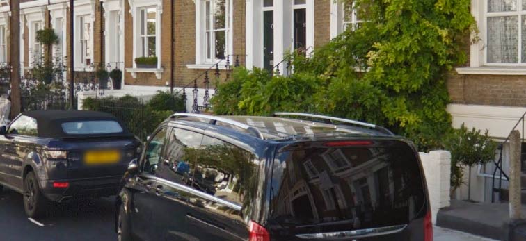 Looking over parked cars to a row of terraced houses.