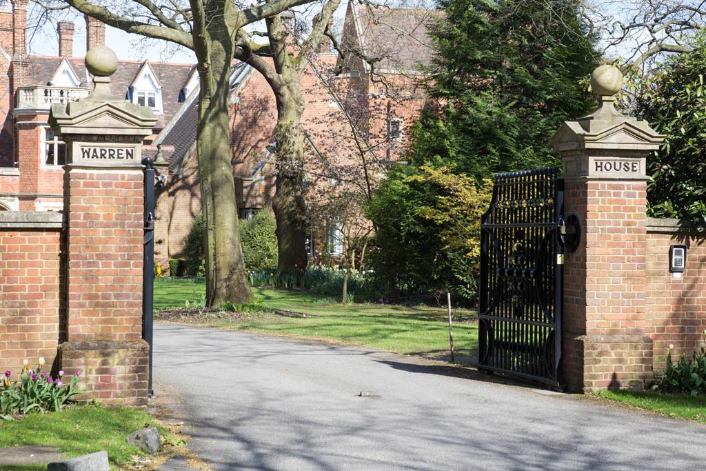 Two brick gate posts, one reading Warren and the other House, with open wrought iron gates leading to a large red brick house.