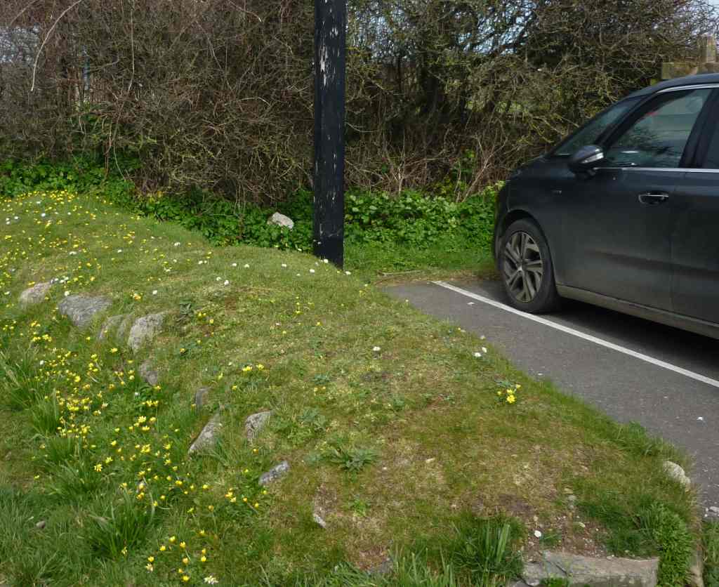 A grassed hillock with a dark coloured car parked by the side.