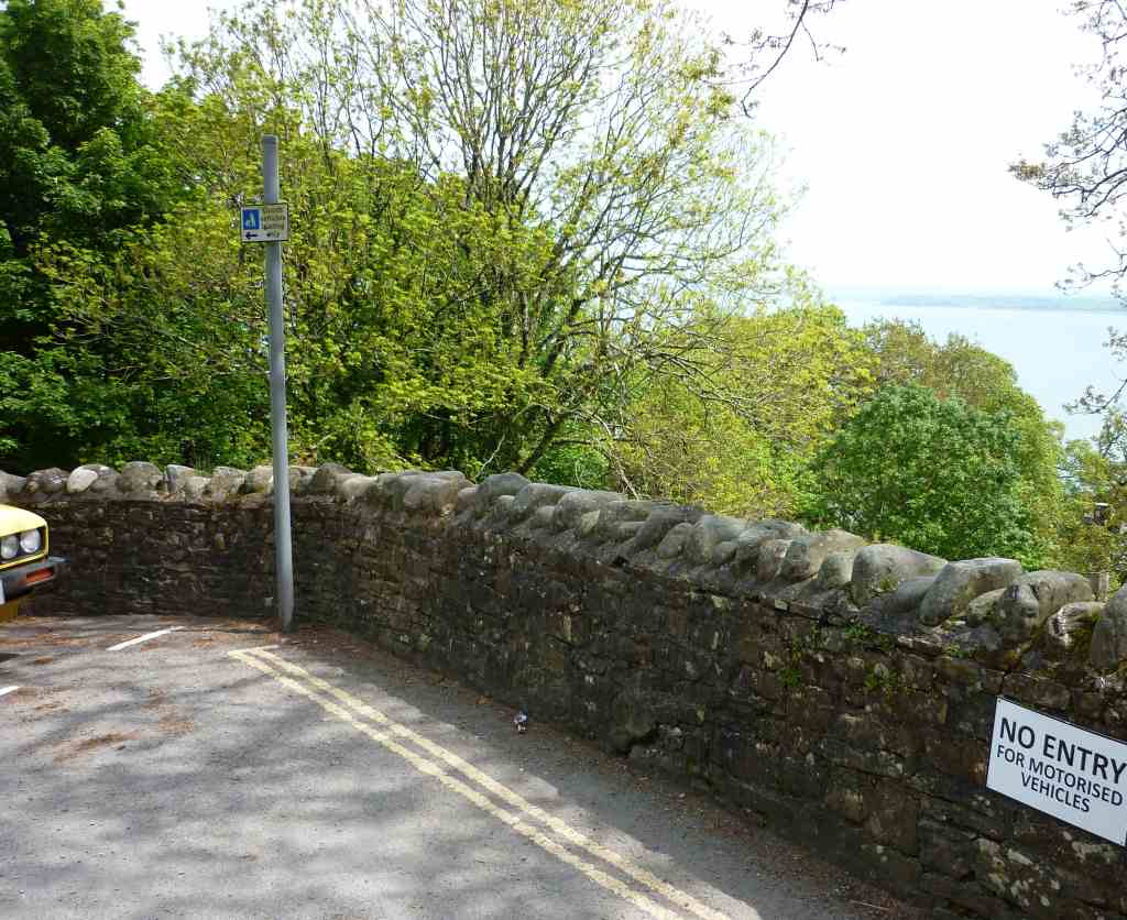Looking over the edge of a stone bridge through trees to the sea beyond
