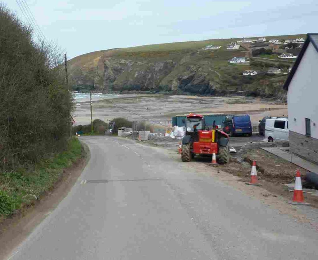Looking down a narrow road that meets a sandy beach, the sea and a grassed cliff beyond.