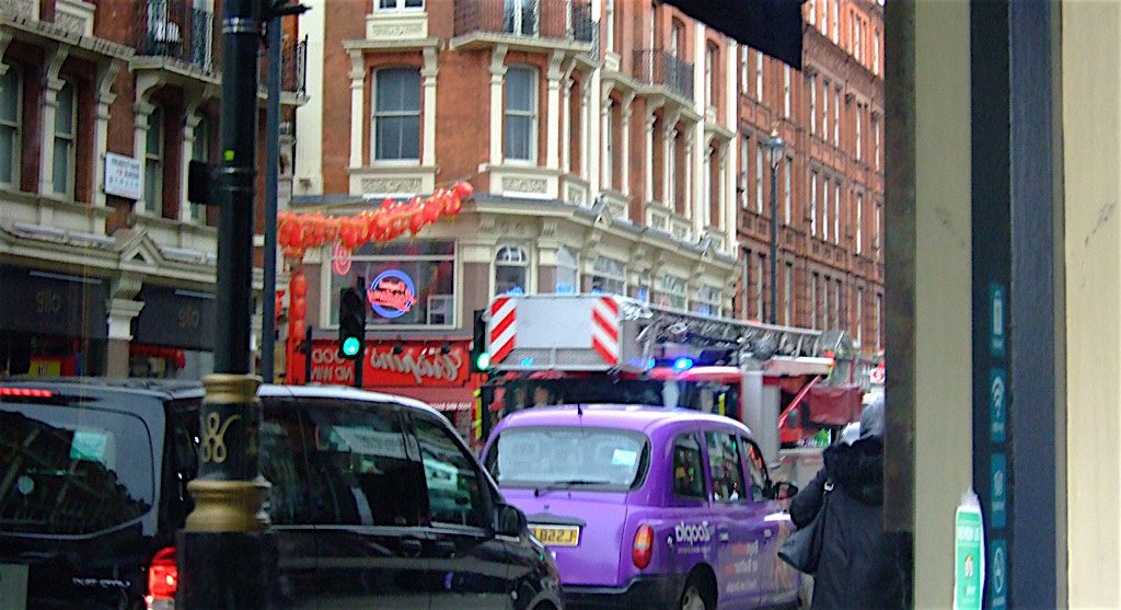 The reflection in the window of 61-63 Shaftesbury Avenue, London W1 (Bella Italia) showing the junction with Macclesfield Street.
