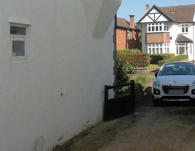 A drive of an house with parked car facing the camera viewing the house on the opposite side of the road.