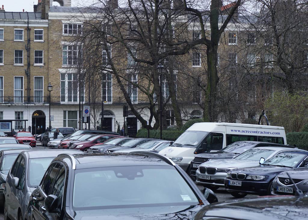 A London Square heavily filled with parked cars and central greenery to the right