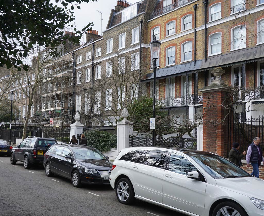 A Regency terrace of homes with walled and gated front gardens and cars parked in the road.