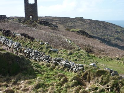 The remains of a stone Cornwall mining engine house on a barren hillside with stone boundary walls
