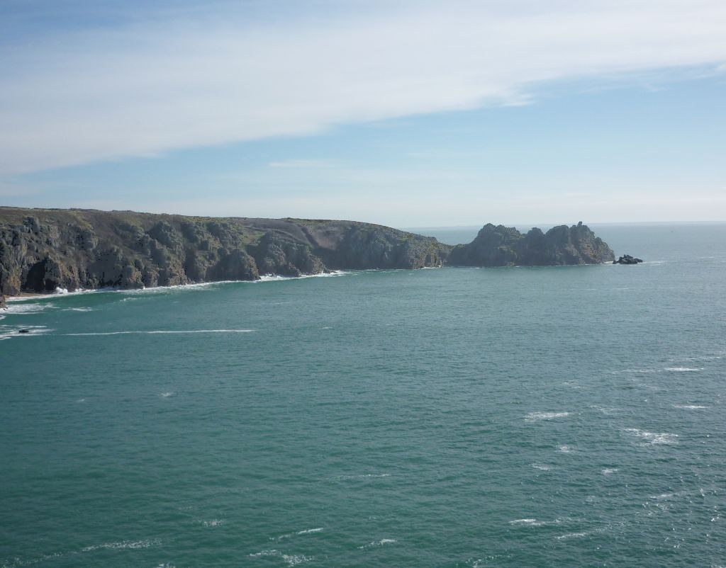 A view of the sea with a narrow green promontory extending from the left out to sea