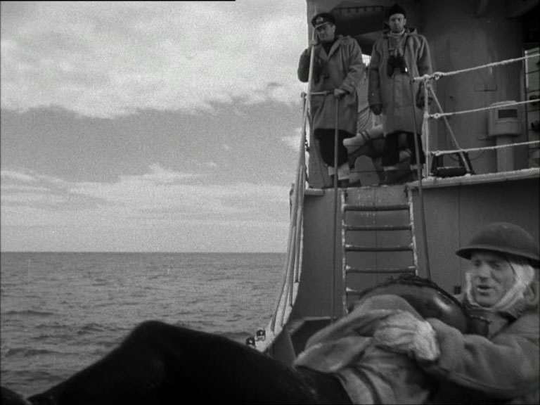 A man with others being pulled aboard a ship in wartime. With two officers looking down from the bridge above.