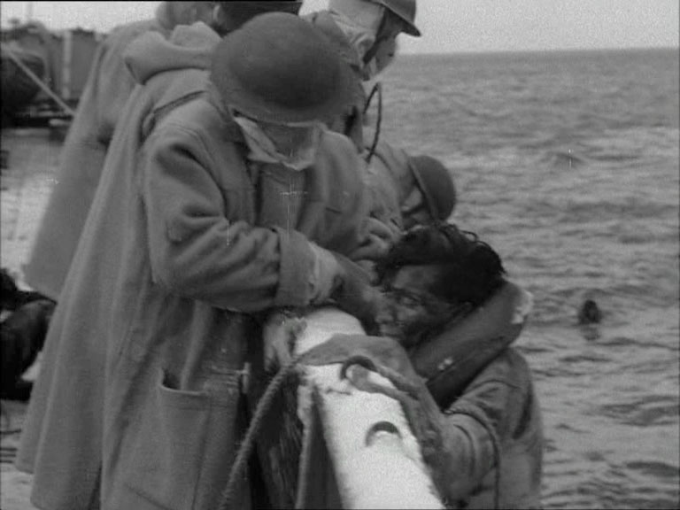 A man with others being pulled aboard a ship in wartime.