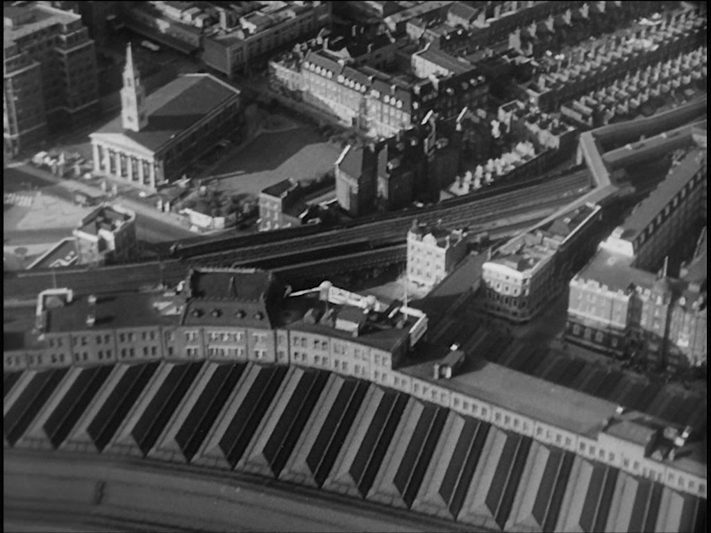 Aerial view of London. The roof of Waterloo Station fills the lower half of the capture but clearly visible on the left hand side is St. John’s Church, 73 Waterloo Road, SE1. To the right of the capture the footbridge leading from Waterloo Station to Waterloo East Station is visible. Circa 1956